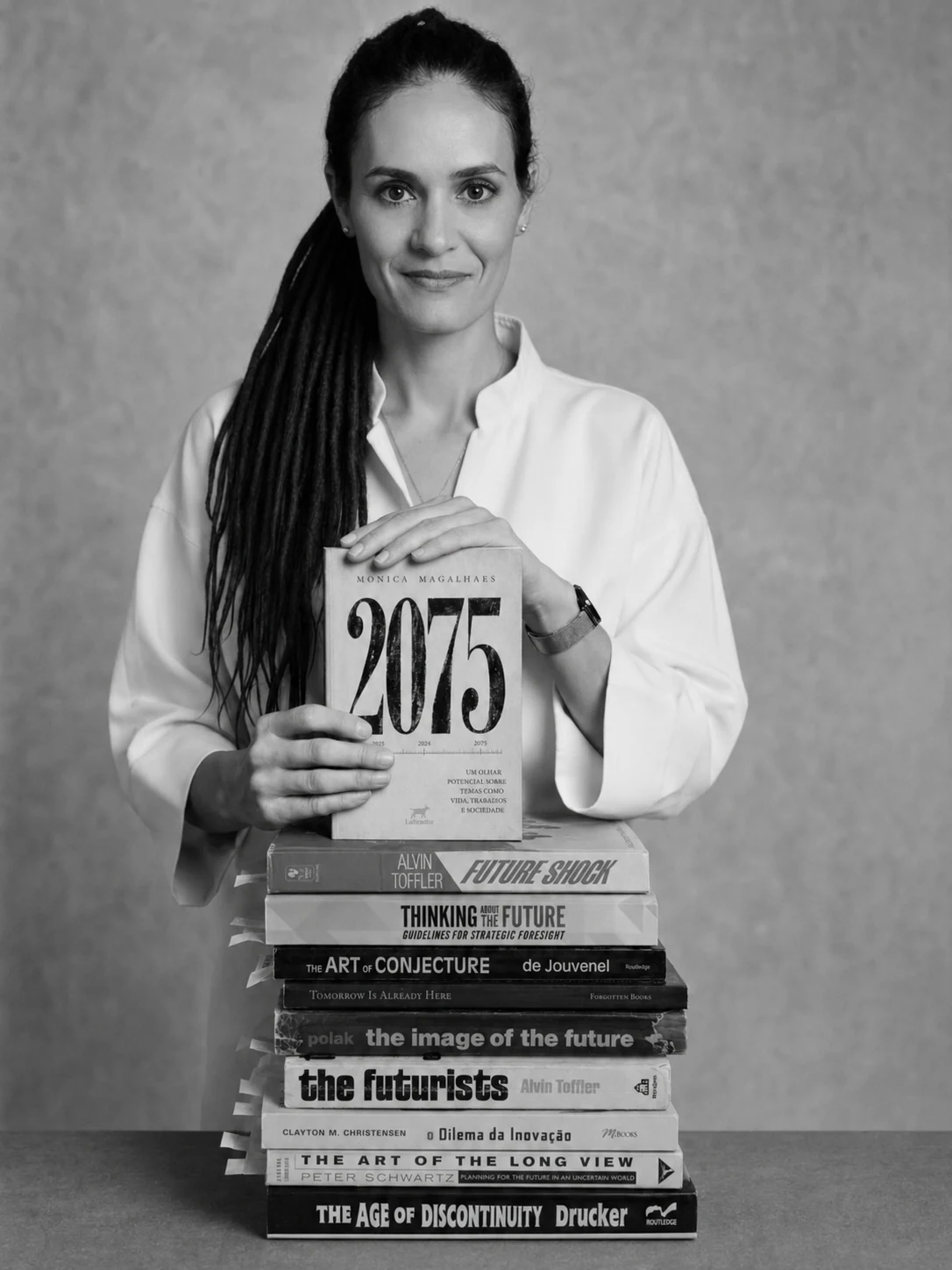 Monica Magalhaes segurando o livro 2075 sobre uma pilha de clássicos do futurismo